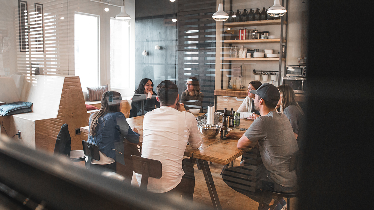 Employees sitting around a common table in a modern office breakroom.